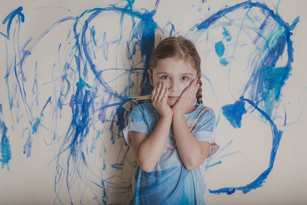 child standing in front of a wall painting holding her face 